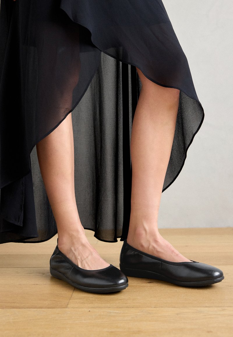 Schwarze Ballerinas aus Leder mit einer runden Spitze und minimalistischem Design, die eine glatte Textur und eine dünne Gummisohle aufweisen.