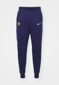 Mörkblå sweatpants i bomullsblandning med elastisk midja, med en tupp-logotyp och Nike-swoosh i guld, avsmalnande ben.