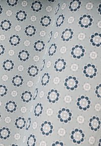 Jasnoniebieska tkanina z powtarzającym się wzorem kwiatowym w kolorze granatowym i białym. Każdy kwiat ma zaokrąglone płatki i centralny kwadratowy wzór.