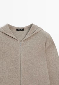 Hellbraune Kapuzenjacke mit Reißverschluss aus weichem Strickstoff, ausgestattet mit einer Kapuze mit Kordelzug und einem minimalistischen Design ohne sichtbare Muster.