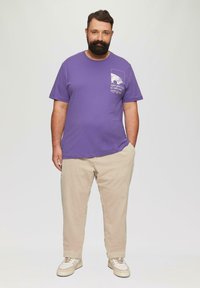 Purple cotton t-shirt with a graphic print on the left chest, paired with beige corduroy pants and beige sneakers.