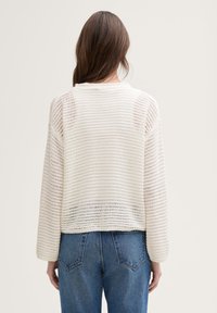 Hvit strikket genser med en teksturert, stripete mønster og en romslig passform. Har lange ermer og rund hals, kombinert med denimbukser.