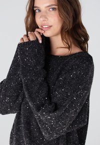 Zwarte gebreide trui met een relaxte fit, versierd met metalen pailletten die over de stof zijn verspreid. Lange mouwen met verlengde boorden.