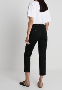 Pantalones recortados negros de textura lisa, con bolsillos traseros y cintura ajustada, combinados con una blusa blanca suelta y sandalias negras.