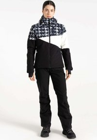 Winterjacke mit einem gemusterten Oberteil in Marineblau und Weiß, einem einfarbigen schwarzen unteren Abschnitt und einem Reißverschluss vorne. Kombiniert mit schwarzen Hosen und Stiefeln.