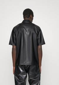 Zwarte leren korte mouwen blouse met een gladde textuur en een klassieke kraag. De achterkant heeft een strak ontwerp zonder logo's of patronen.