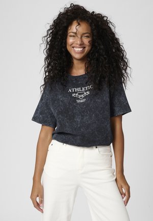 Ciemnoszara, krótki rękaw, koszulka typu crew neck z zatarciem, z nadrukowanym białym tekstem "ATHLETIC" oraz emblematem. Połączona z białymi dżinsami bawełnianymi.