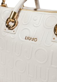 Hvid textured læder håndtaske med prægede "LIU•JO" mønster, guld metal logo, lynlås og håndtag vedhæftninger.