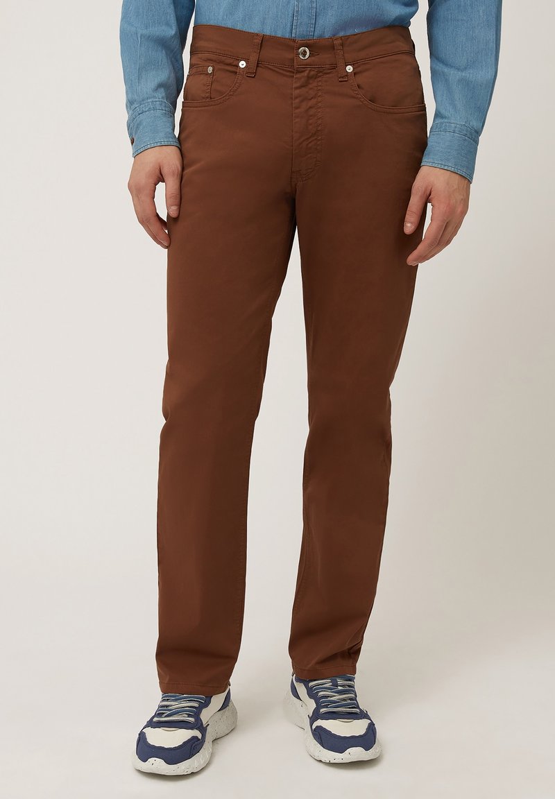 Pantaloni di cotone marroni con vestibilità dritta, cinque tasche e accessori metallici. Abbinati a sneaker bianche e blu.