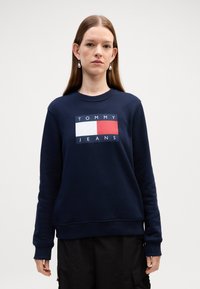 Felpa blu navy realizzata in misto cotone, caratterizzata da una grafica rettangolare con "TOMMY" in bianco e "JEANS" sotto in testo bianco.
