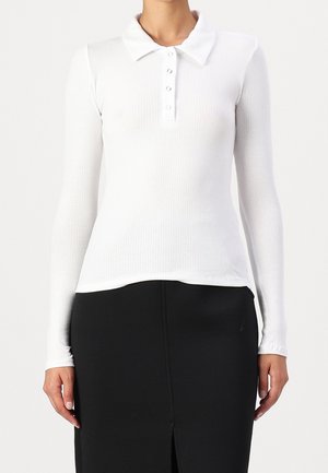 Valkoinen pitkähiha polo-paita, jolla on ribbikuviointi, viiden napin läppä ja terävä kaulus. Täydentää mustaa hametta, jossa on etuhaalari.