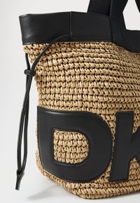 Bolsa de palha entrelaçada com detalhes em pele preta e um grande logótipo DK. Possui um fecho de cordão e alças pretas resistentes.