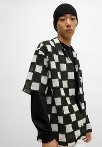 Paita lühikeste varrukatega must-valge ruuduline kujundus, millel on lahtine kudumisteksteen, ja all on solidne must pikkade varrukatega särk.