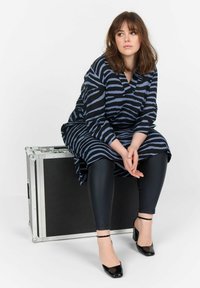 Mustra mustriline kätisega tuunikakleit, mille värvid on must ja sinine, kombineeritud mustade leggingside ja kontsakingadega, istudes hõbedasel kotil.