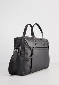 Black leather bag with dual top handles, adjustable shoulder strap, front zipper pocket, smooth texture, and clean minimalist design.