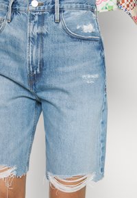 Shorts de mezclilla azul claro con dobladillos deshilachados, detalles desgastados en los bolsillos y un diseño de cintura alta.