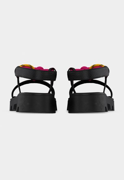 Μαύρα πλατφόρμα σανδάλια με χοντρές σόλες, λουράκια στον αστράγαλο και ορατά ροζ και κίτρινα επενδεδυμένα πέλματα, εμφανιζόμενα από πίσω.