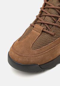 Sneaker in camoscio marrone e mesh con tomaia testurizzata, puntale rinforzato e suola in gomma nera con lacci e occhielli marroni.