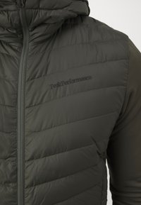 Groene puffervest met horizontale stiksels, ritssluiting en logo van Peak Performance. Lichtgewicht materiaal, gladde textuur en met capuchon.