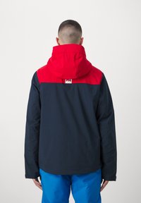Wasserdichte Jacke mit rotem oberen Teil und dunkelblauem unteren Teil, verstellbarer Kapuze, langen Ärmeln und einem Logotag auf dem Rücken.