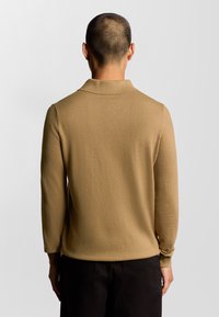 Beige långärmad polo shirt med mjuk textur och ribbad krage, med en enfärgad design och avslappnad passform. Enkelt bakvy.