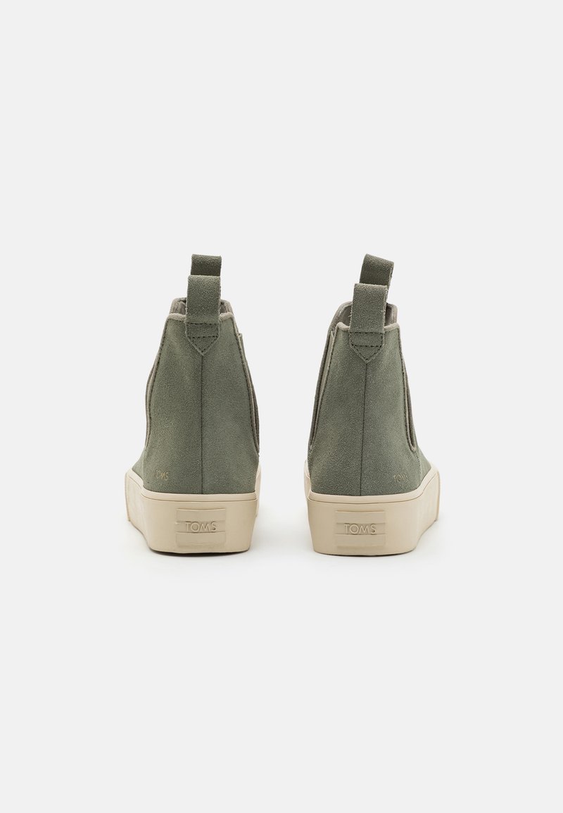 Oliwkowe zamszowe botki za kostkę z beżowymi gumowymi podeszwami, z tylnymi uchwytami i minimalistycznym designem. Logo TOMS wytłoczone z boku.