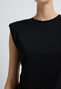 Černý top bez rukávů s ramínky, kulatým výstřihem a hladkou texturou; látka se zdá být elastická a přiléhavá.