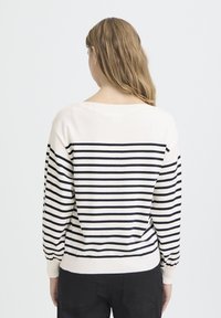 Pull crème à rayures noires, manches longues et poignets côtelés. Coupe décontractée et encolure large. Matière en tricot texturé.