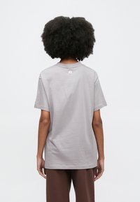 Svetlosivé tričko z bavlny s krátkymi rukávmi, okrúhlym výstrihom a malým logom na zadnej strane. Mäkká textúra a voľný strih.