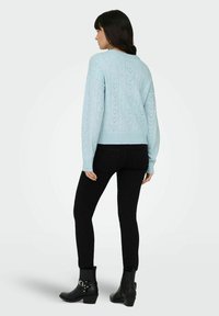 Pull bleu clair en maille avec un motif cœur texturé, ourlet et poignets côtelés, porté avec un jean skinny noir et des bottines noires.