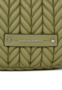 Grønn quiltet skinnhåndveske med chevronmønster, svarte detaljer og sølvfarget tilbehør som viser merkevaren.