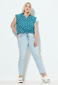 Tummansininen pusero, jossa on valkoinen geometrinen kuvio, solmittu vyötärölle; yhdistetty vaaleansinisiin farkkuihin ja valkoisiin korkokenkiin. Silkkinen pinta.