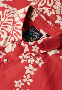 Camisa roja abotonada con estampado floral blanco, con cuello clásico y detalles en la etiqueta. Hecha de tela ligera.