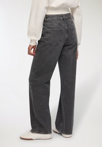 Jeans a vita alta e gamba larga in denim grigio scuro con finitura testurizzata, dotati di due tasche posteriori e dettagli di cucitura discreti.