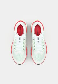 Világoszöld Nike futócipők piros részletekkel és fehér fűzőkkel, felülnézetből, sima fehér háttér előtt.