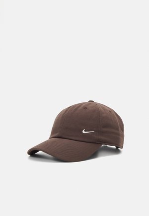 Gorra de béisbol marrón con visera curva y logo blanco de Nike en la parte frontal, mostrada sobre un fondo blanco liso.