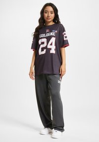Svart oversized t-skjorte med "COLOGNE" og "24" i hvite bokstaver. Sammen med grå joggebukser og hvite sneakers. Enkelt, sporty design.