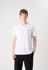 Λευκό βαμβακερό μπλουζάκι με κοντά μανίκια, χαρακτηρισμένο με ένα μικρό μαύρο λογότυπο στο αριστερό στήθος; συνδυασμένο με μαύρο παντελόνι. Λείος υφασμάτινος τύπος.