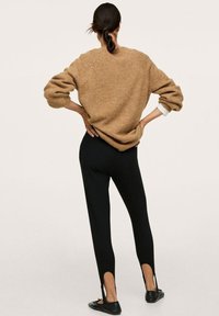 Chunky beżowy sweter z balonowymi rękawami, zestawiony z dopasowanymi czarnymi legginsami z wycięciami. Czarne baleriny dopełniają stylizację.