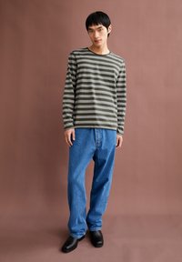 Grijs en olijfgroen gestreepte lange mouwen shirt met ronde hals, gecombineerd met losse blauwe denim jeans en zwarte schoenen. Soepele stoftextuur.