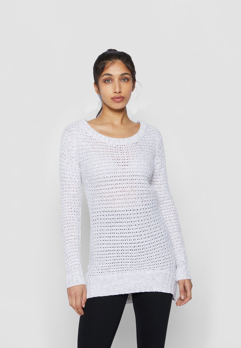 Pull en tricot blanc à manches longues avec un motif de tissage lâche. Il dispose d'un décolleté large et de poignets côtelés. Assorti à des leggings noirs.