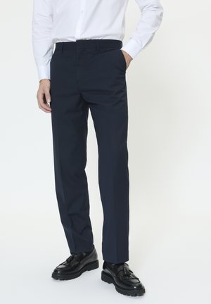 Marineblå bukser lavet af glat stof med en skræddersyet pasform, der har sidelommer og en flad front, kombineret med sorte sko.