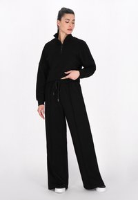 Svart zip-up hoodie med hög krage och breda ärmar, i kombination med lösa svarta sweatpants med dragsko och sidofickor.