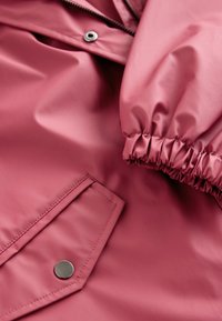Rózsaszín vízálló dzseki, csillogó textúrával, rugalmas mandzsettákkal és patentos zsebbel. Cipzár az elején, sima kivitelben.