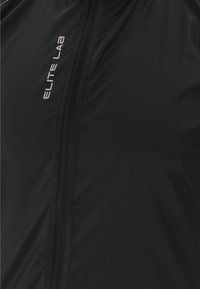 Schwarze leichte Jacke aus glattem Stoff mit subtiler gerippter Textur. Mit vollem Reißverschluss und silbernem "ELITE LAB" Logo.