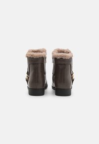 Bottines en cuir marron avec doublure en faux fourrure, zips sur les côtés et semelles plates, présentant des accents en métal doré sur les côtés.