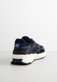 Navy blue sports shoe featuring mesh and suede materials, a thick white sole with textured patterns, and a blue fabric accent on the heel.