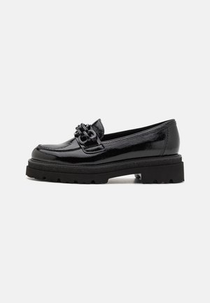 Mocassin noir brillant avec semelle crantée épaisse et bride tressée décorative sur le dessus, présenté en profil sur fond uni.