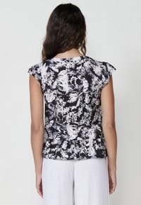 Čierno-biely vzorovaný top s krátkymi, riasenými rukávmi a voľným strihom. Mäkká tkanina s detailom peplum na spodku.