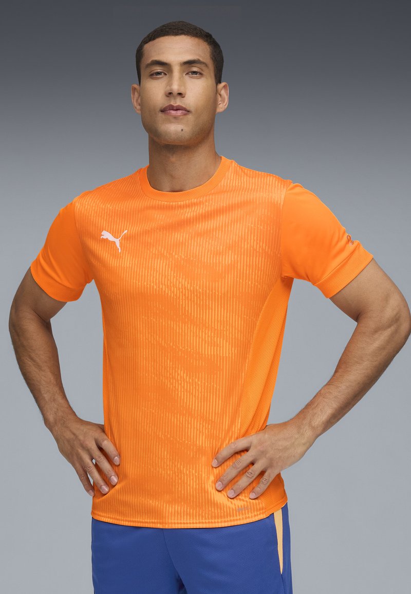 Maglia sportiva arancione con un motivo testurizzato, maniche corte, colletto a girocollo e logo bianco sul lato sinistro del petto, abbinata a pantaloni corti blu.